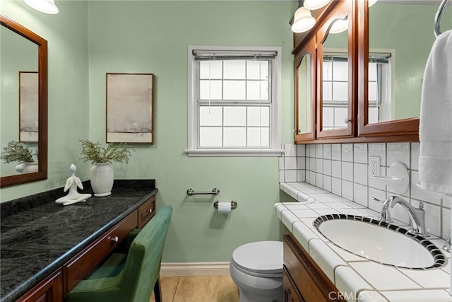 bathroom featuring toilet, decorative backsplash, vanity, tile patterned flooring, and baseboards