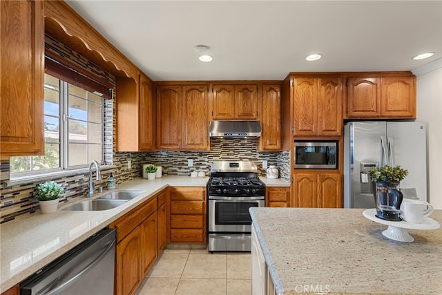 kitchen featuring range hood, light countertops, appliances with stainless steel finishes, brown cabinetry, and a sink