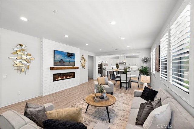 living area featuring baseboards, light wood-type flooring, a glass covered fireplace, and recessed lighting