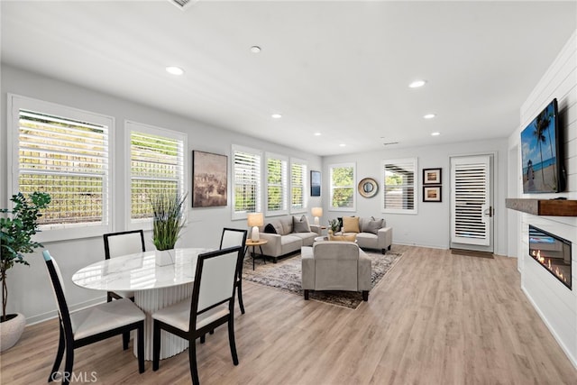 living room featuring a glass covered fireplace, baseboards, light wood finished floors, and recessed lighting