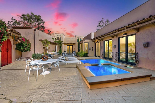 pool at dusk featuring a patio and an in ground hot tub