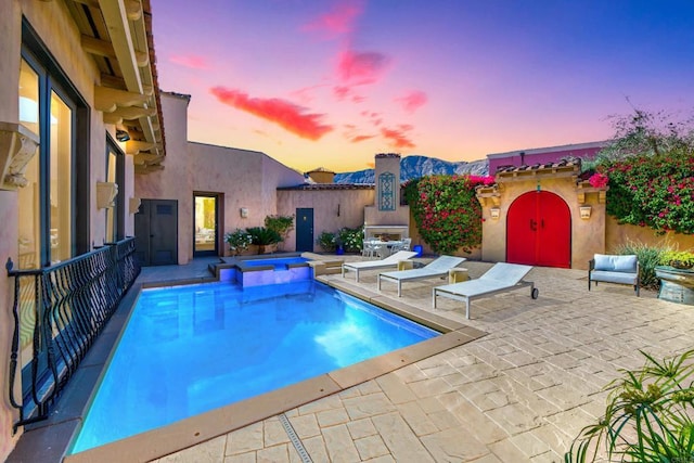 pool at dusk featuring a fenced in pool, an in ground hot tub, and a patio