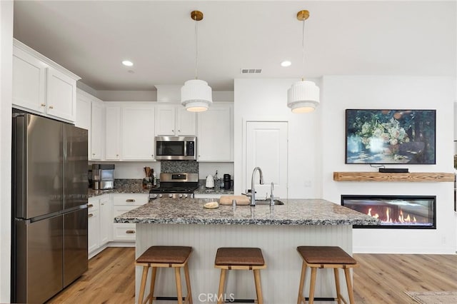 kitchen with appliances with stainless steel finishes, a kitchen bar, a sink, and white cabinetry