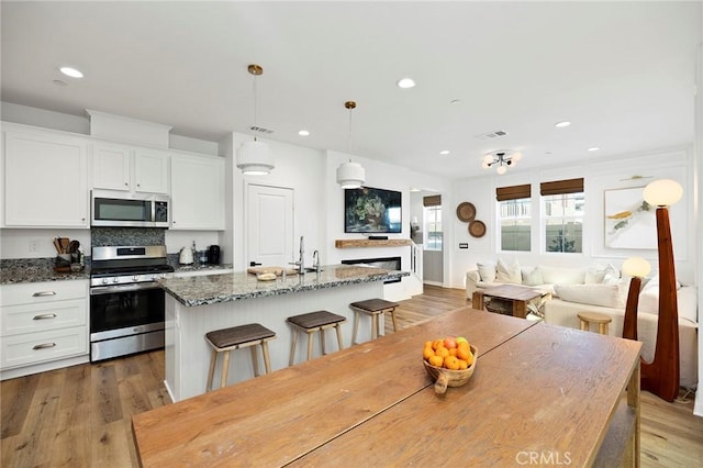 kitchen featuring visible vents, an island with sink, light wood-style flooring, appliances with stainless steel finishes, and white cabinetry