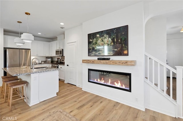 kitchen with light stone counters, decorative light fixtures, light wood finished floors, stainless steel appliances, and white cabinets