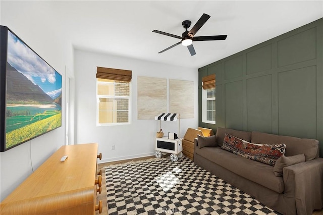 living area featuring baseboards, a ceiling fan, and a decorative wall