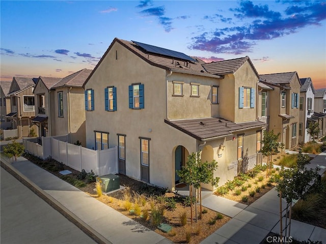 view of front of home featuring solar panels, fence, a tiled roof, and stucco siding