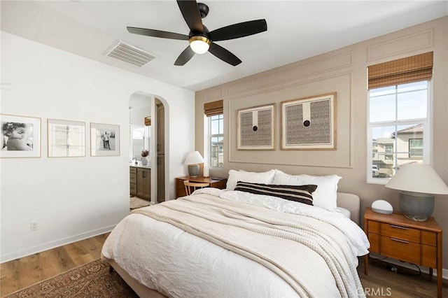 bedroom with arched walkways, ensuite bathroom, visible vents, baseboards, and light wood-type flooring