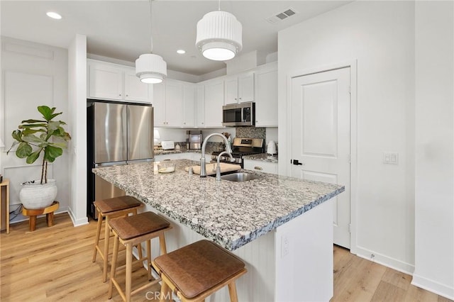 kitchen featuring stainless steel appliances, light wood finished floors, white cabinetry, and a kitchen breakfast bar