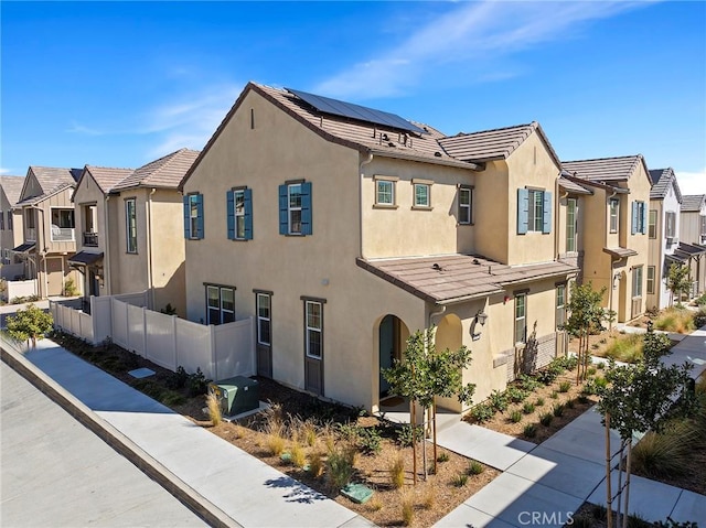 multi unit property with solar panels, a tile roof, a residential view, fence, and stucco siding