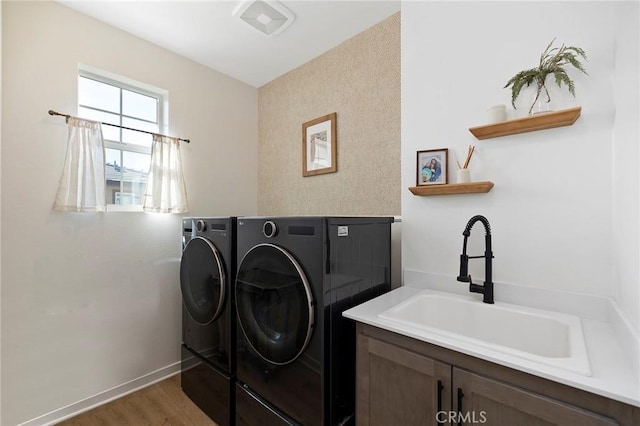 clothes washing area featuring cabinet space, baseboards, light wood-type flooring, washing machine and dryer, and a sink