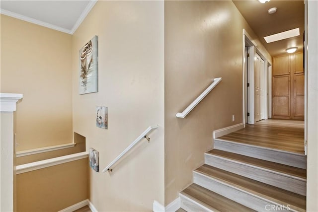 stairway with wood finished floors, baseboards, and ornamental molding