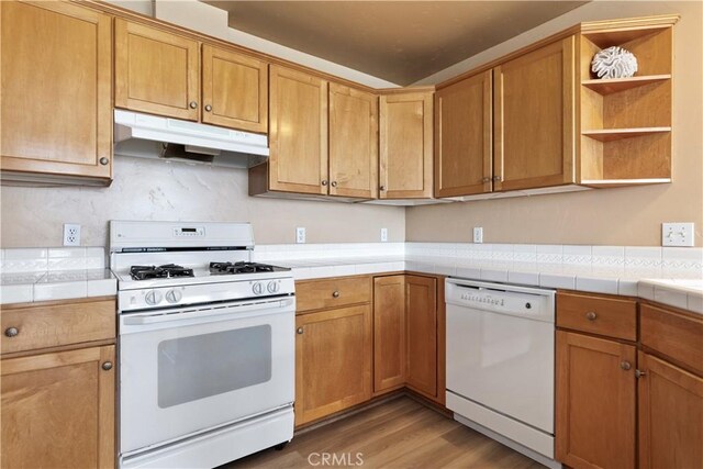 kitchen with under cabinet range hood, open shelves, white appliances, light wood-style floors, and brown cabinetry