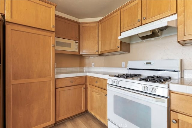 kitchen with white appliances, tile counters, light wood finished floors, and under cabinet range hood