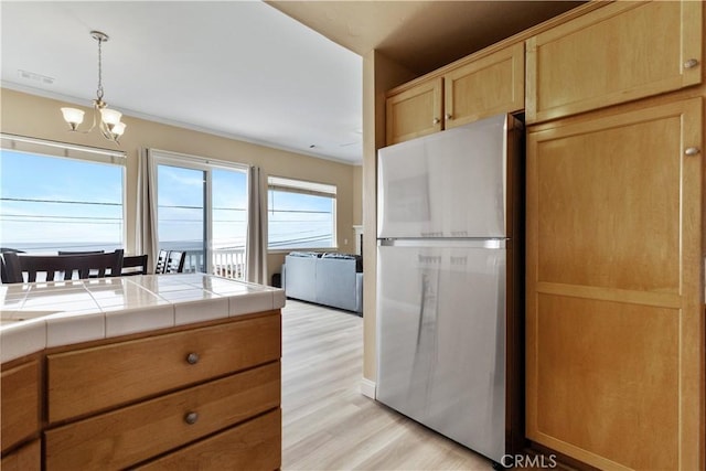 kitchen with a notable chandelier, light wood-style flooring, light brown cabinets, freestanding refrigerator, and tile countertops