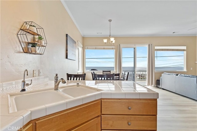 kitchen with decorative light fixtures, light wood-type flooring, crown molding, and a sink