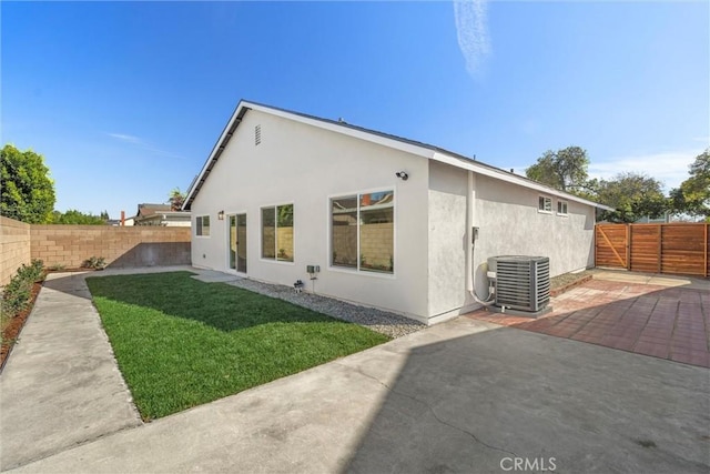 back of house with a patio, central AC unit, a fenced backyard, a yard, and stucco siding