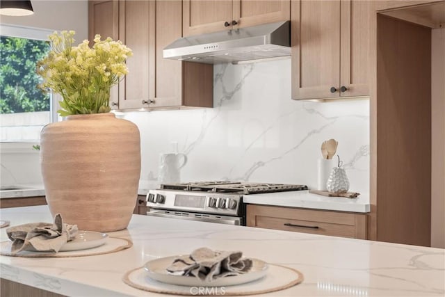 kitchen featuring gas stove, backsplash, under cabinet range hood, and light stone countertops