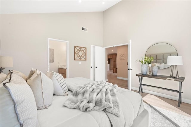 bedroom featuring visible vents, ensuite bathroom, wood finished floors, high vaulted ceiling, and baseboards