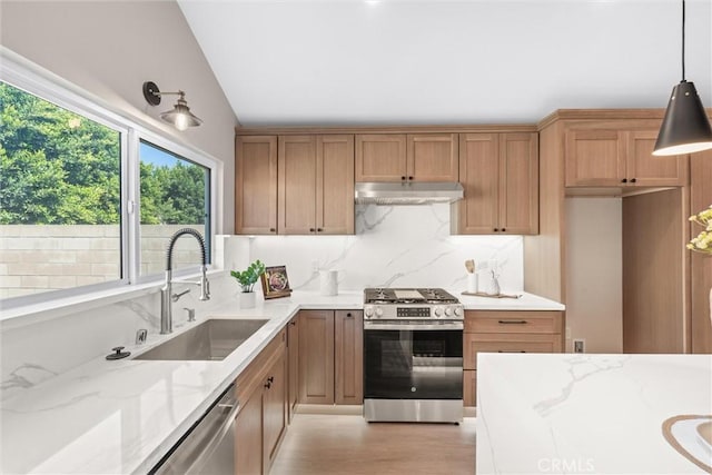 kitchen with tasteful backsplash, appliances with stainless steel finishes, light stone countertops, under cabinet range hood, and a sink