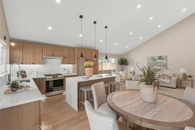 kitchen with gas range, under cabinet range hood, open floor plan, and a sink