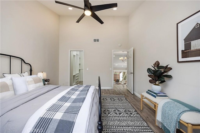 bedroom featuring recessed lighting, wood finished floors, a towering ceiling, visible vents, and baseboards