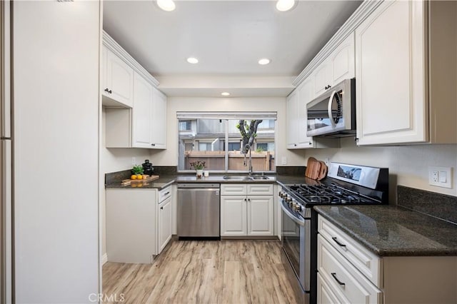 kitchen featuring light wood finished floors, white cabinets, stainless steel appliances, a sink, and recessed lighting