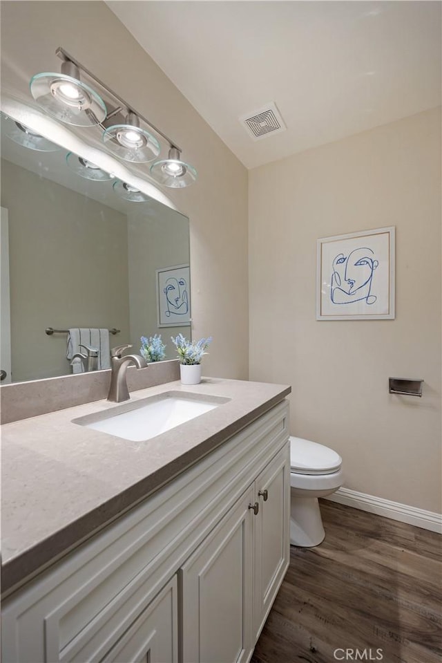 bathroom featuring visible vents, toilet, vanity, wood finished floors, and baseboards