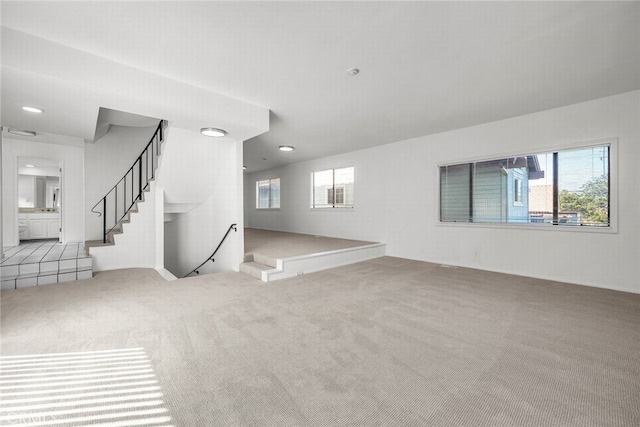 unfurnished living room with carpet floors, a wealth of natural light, and stairs