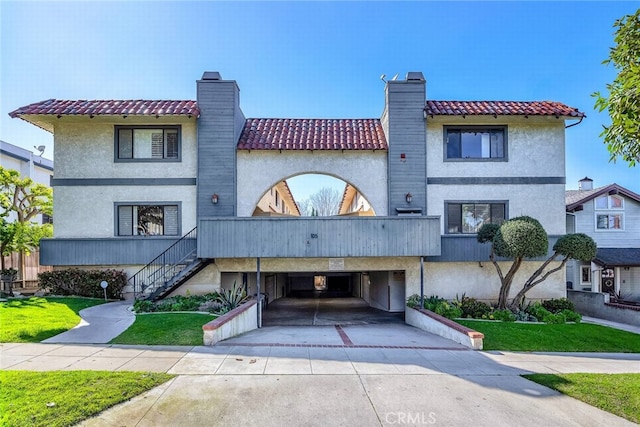 view of front of house with a chimney, concrete driveway, a carport, a tiled roof, and stairs