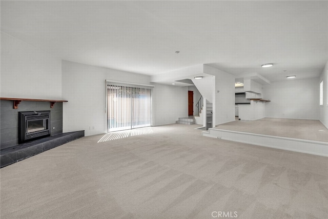 unfurnished living room featuring a tile fireplace, stairway, and carpet