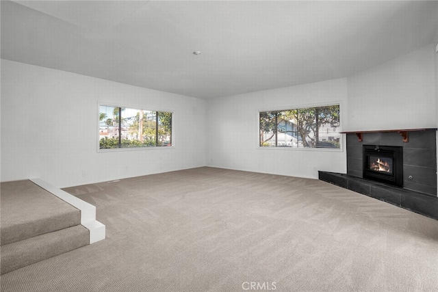 unfurnished living room featuring a wealth of natural light, carpet, and a tiled fireplace