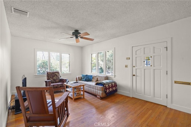 living area with baseboards, visible vents, a ceiling fan, light wood-style flooring, and a textured ceiling