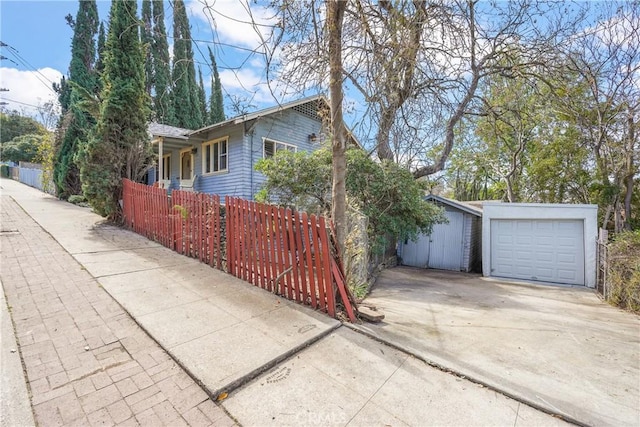 view of home's exterior featuring an outbuilding, concrete driveway, a fenced front yard, and an attached garage