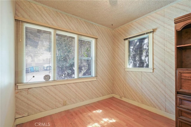 empty room with plenty of natural light, crown molding, a textured ceiling, and wood finished floors