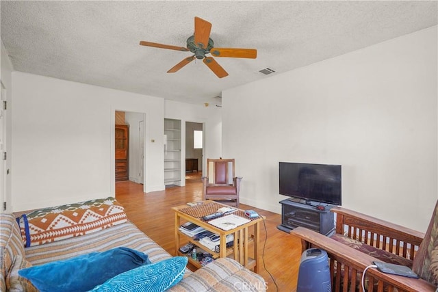 living area with a ceiling fan, visible vents, a textured ceiling, and wood finished floors