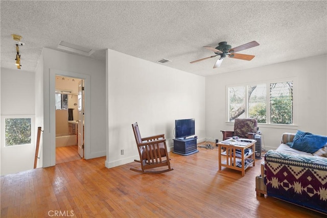 living area with attic access, visible vents, baseboards, hardwood / wood-style flooring, and a textured ceiling