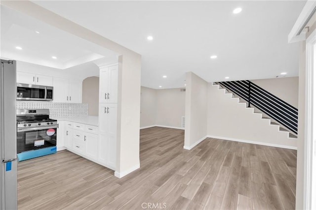 kitchen featuring light wood-type flooring, stainless steel appliances, decorative backsplash, and open floor plan