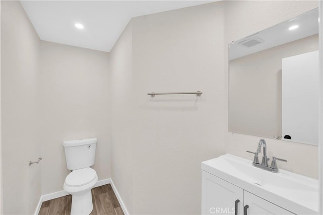 half bath featuring toilet, wood finished floors, visible vents, vanity, and baseboards