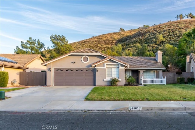 view of front facade with a tiled roof, stucco siding, concrete driveway, and fence