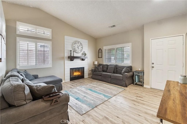 living area featuring visible vents, lofted ceiling, light wood-style floors, and a glass covered fireplace