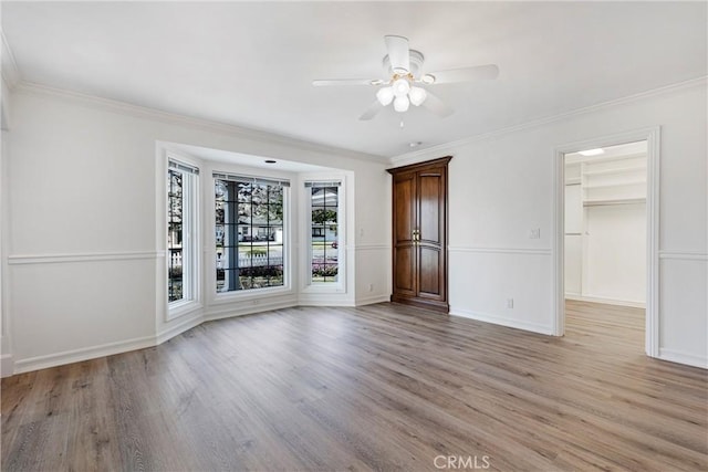 spare room with light wood-style floors, baseboards, a ceiling fan, and crown molding