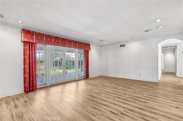 spare room with arched walkways, wood finished floors, visible vents, baseboards, and crown molding