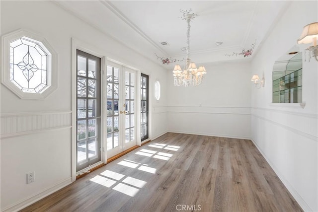 unfurnished dining area with french doors, a notable chandelier, crown molding, and wood finished floors