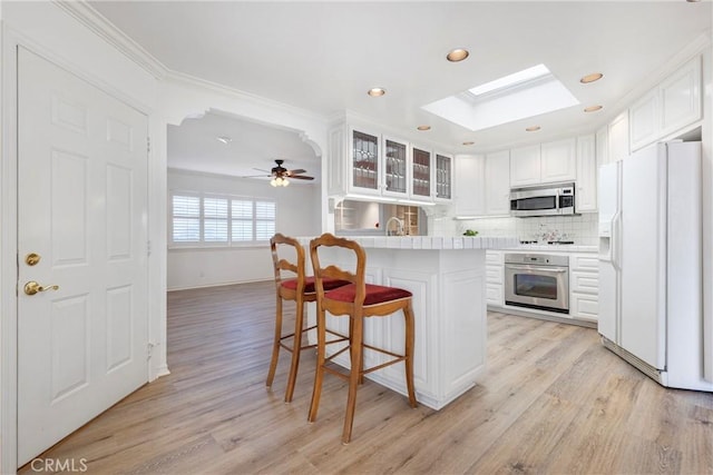 kitchen with a skylight, glass insert cabinets, appliances with stainless steel finishes, a kitchen breakfast bar, and backsplash