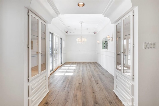 interior space with french doors, a wainscoted wall, crown molding, a notable chandelier, and light wood-type flooring