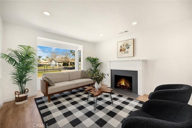 living area featuring light wood finished floors, baseboards, visible vents, a brick fireplace, and recessed lighting