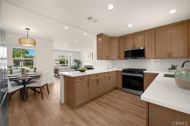 kitchen featuring visible vents, stainless steel microwave, a peninsula, black gas stove, and a sink