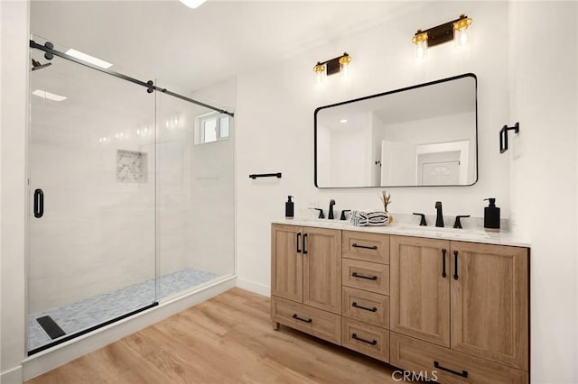 bathroom with double vanity, a sink, a shower stall, and wood finished floors