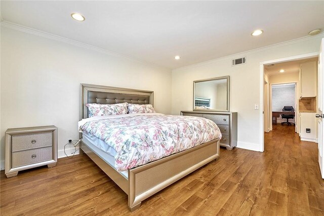 bedroom featuring ornamental molding, visible vents, baseboards, and wood finished floors